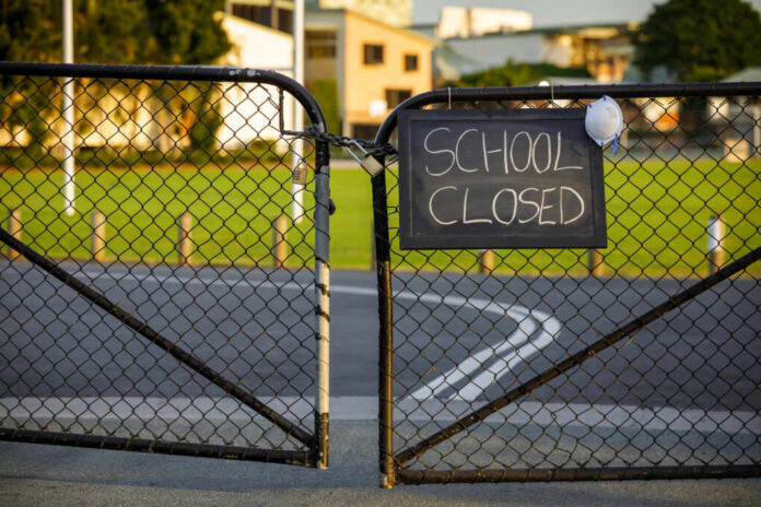 School,Closed,Sign,With,Protective,Mask,Hanging,On,A,Padlocked