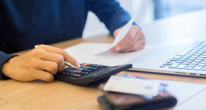 Man,Hand,Write,On,Notebook,And,Calculate,On,Calculator,About