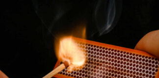 A hand striking a match against a matchbox, igniting it with flames and smoke