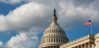 The U.S. Capitol building with a dome and American flag under a cloudy sky