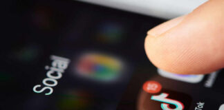 Close-up of a finger tapping a TikTok icon on a smartphone screen with social media labels