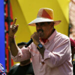 A man in a straw hat passionately speaking into a microphone at a lively outdoor event