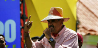 A man in a straw hat passionately speaking into a microphone at a lively outdoor event