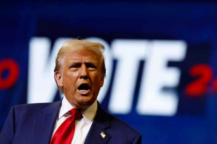 A man passionately speaking at a campaign event with a VOTE backdrop