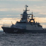 A military ship sailing on the ocean at sunset with crew members visible on deck