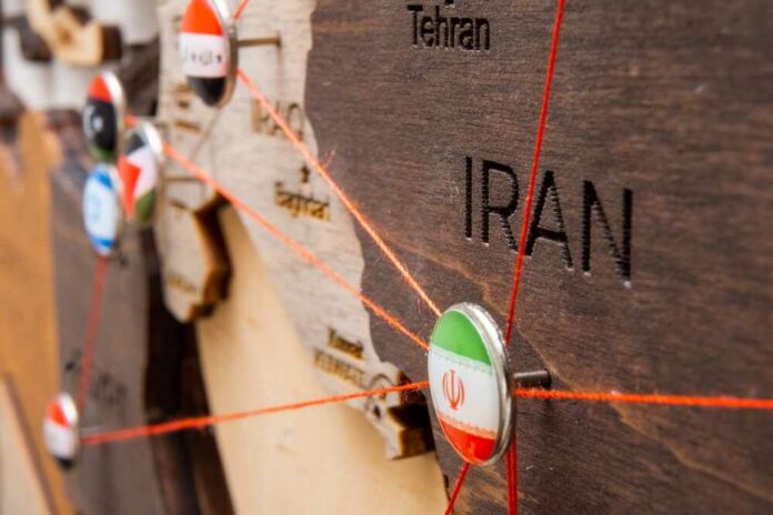 Close-up of a wooden map highlighting Iran with travel pins and red strings