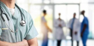 A healthcare professional in scrubs with a stethoscope, standing with arms crossed in a hospital setting
