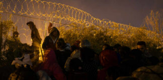 A crowd of migrants gathered near a barbed wire fence at night