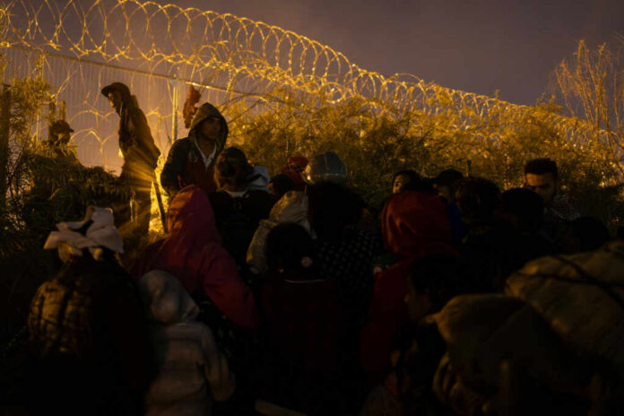 A crowd of migrants gathered near a barbed wire fence at night