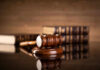A wooden gavel resting on a round base with law books in the background
