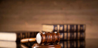 A wooden gavel resting on a round base with law books in the background
