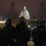 Police officers in riot gear standing in front of the Capitol building at night