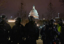 Police officers in riot gear standing in front of the Capitol building at night