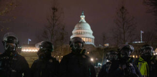 Police officers in riot gear standing in front of the Capitol building at night
