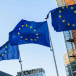Three European Union flags waving against a clear blue sky