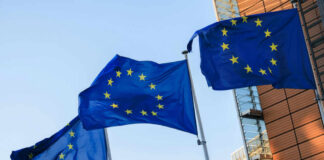Three European Union flags waving against a clear blue sky