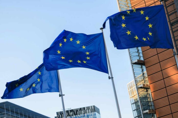 Three European Union flags waving against a clear blue sky