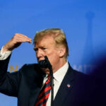 A public figure gesturing while speaking into a microphone on stage