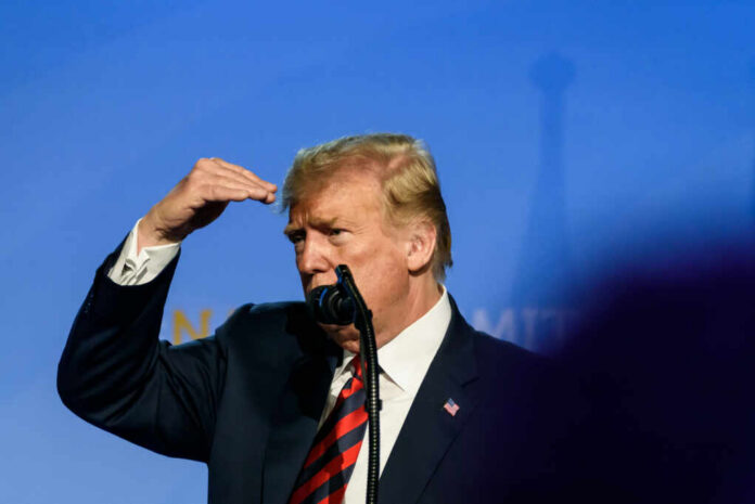 A public figure gesturing while speaking into a microphone on stage