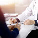 A doctor writing notes during a consultation with a patient