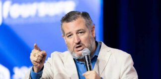A man in a light suit passionately speaking into a microphone at a conference