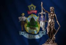 Bronze statue of Lady Justice in front of the Maine state flag