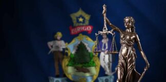 Bronze statue of Lady Justice in front of the Maine state flag