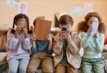Four children sitting together, each engaged with their electronic devices