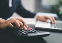 A business professional using a calculator while working on a laptop