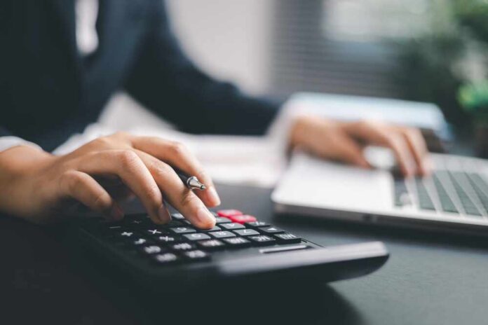 A business professional using a calculator while working on a laptop