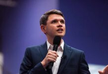 A man in a suit speaking into a microphone at a conference
