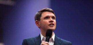 A man in a suit speaking into a microphone at a conference
