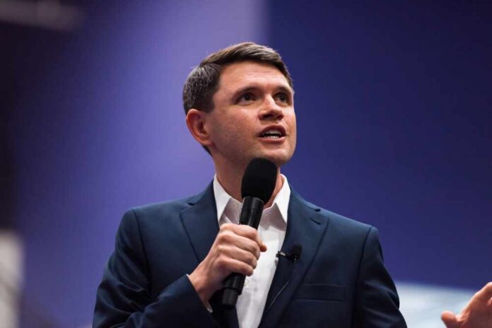 A man in a suit speaking into a microphone at a conference