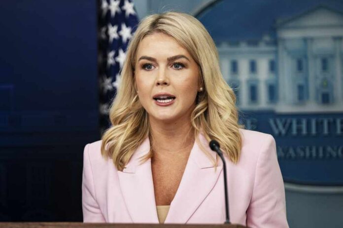 A woman in a pink blazer speaking at a podium during a press briefing