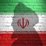 New Iranian Leader’s Vow: Endless Vengeance Ahead Silhouette of a figure against the Iranian flag painted on a brick wall