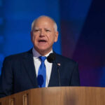 A man in a suit speaking at a podium with a microphone