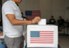 Person casting a vote into a ballot box with an American flag