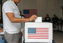 Person casting a vote into a ballot box with an American flag