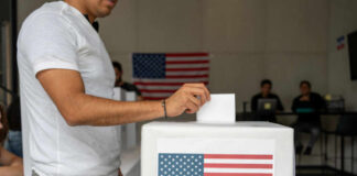 Person casting a vote into a ballot box with an American flag