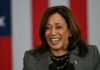 A woman smiling while speaking at a podium with an American flag backdrop
