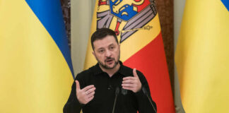 Ukrainian leader delivering a speech at a podium with national flags in the background