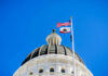 View of a state capitol dome with American and California flags against a blue sky