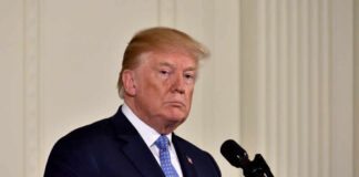 A political figure standing at a microphone with a serious expression