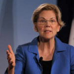 A woman in a blue blazer speaking passionately at a podium