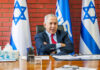 A political leader seated at a desk with Israeli flags in the background