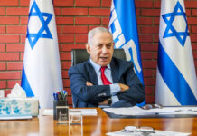 A political leader seated at a desk with Israeli flags in the background