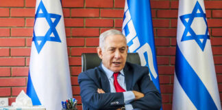 A political leader seated at a desk with Israeli flags in the background
