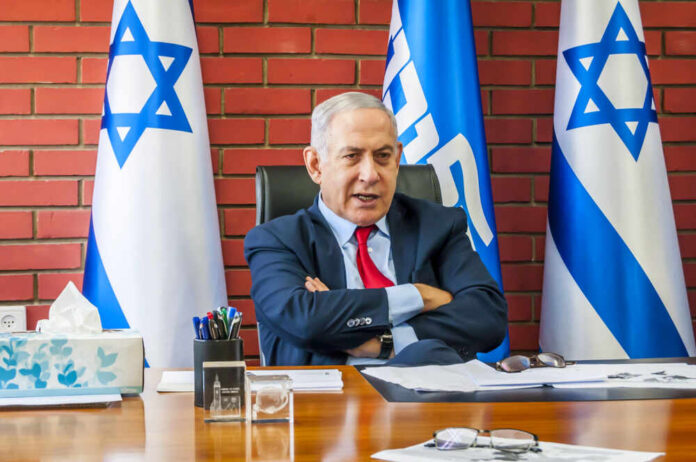 A political leader seated at a desk with Israeli flags in the background