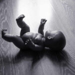 A black and white image of a doll lying on a wooden floor