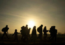 Silhouetted group of refugees walking towards the sunset